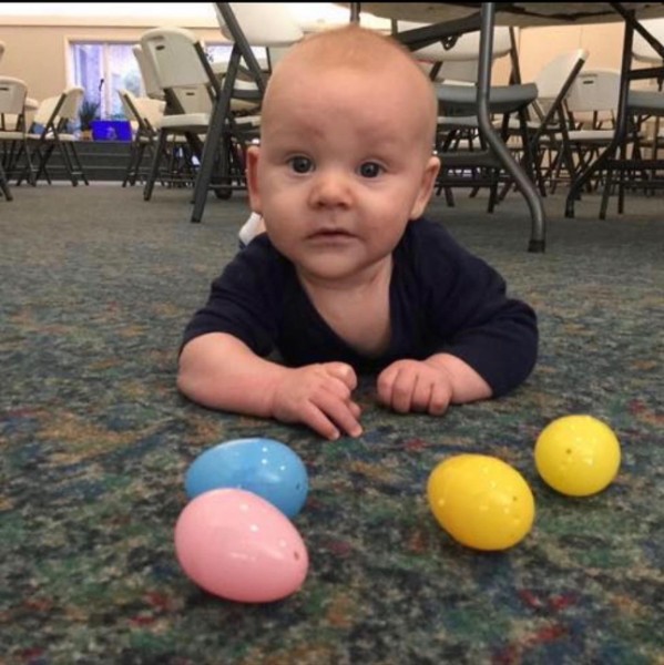 A baby on the floor reaching for colourful plastic Easter eggs