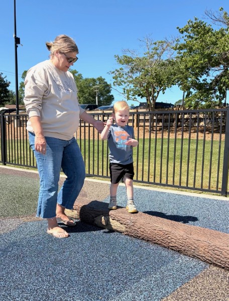 An early interventionist helping a young child balance while walking across a log outdoors